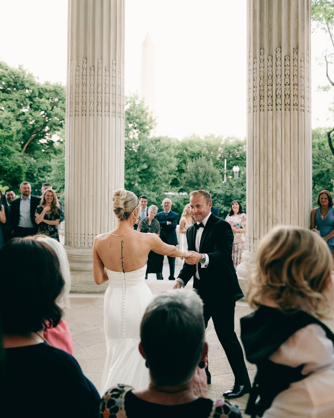 The couple walking out hand in hand through their guests, between the columns of the terrace