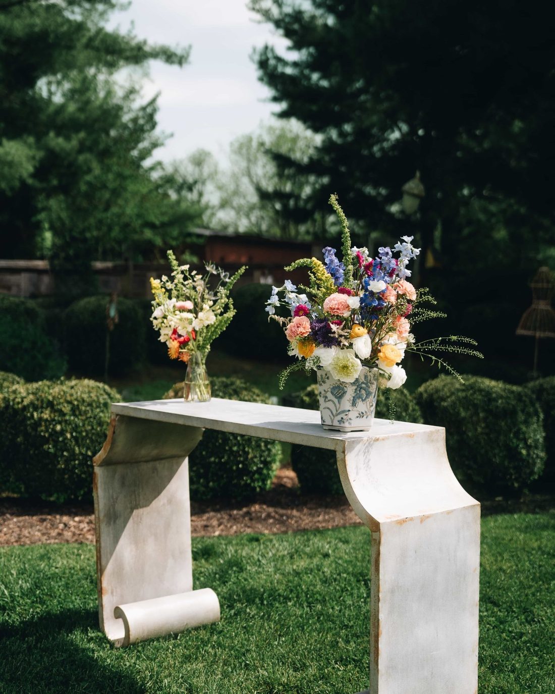 Two vases of wildflowers on a curved stone console set out on the grass
