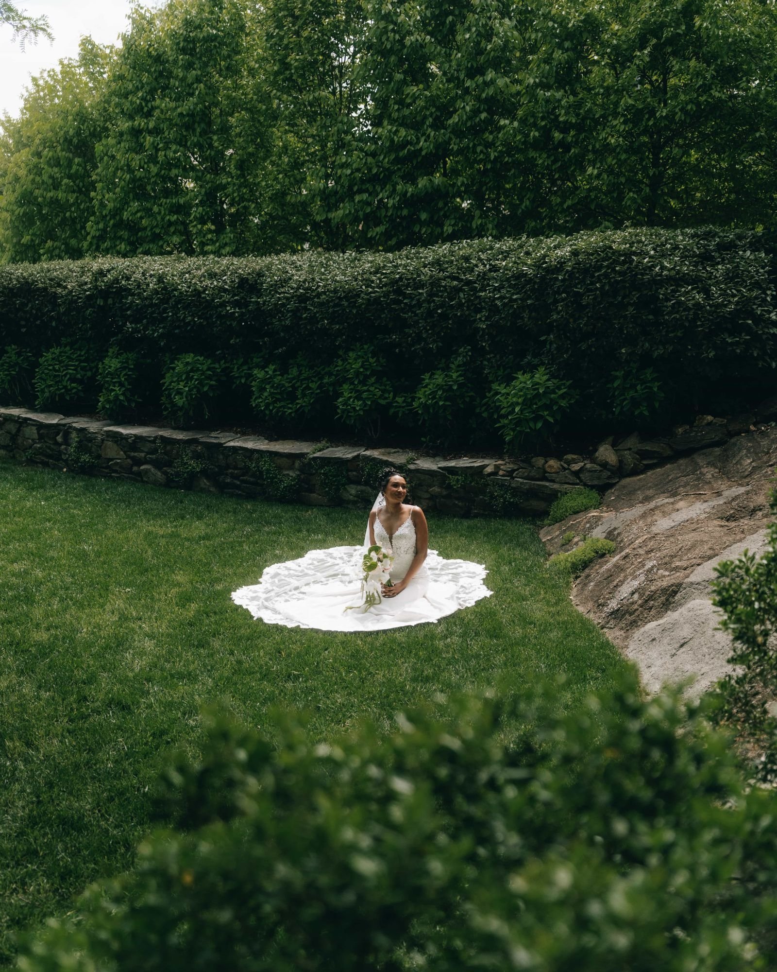 A bride sitting alone on a lawn with her gown spread in a circle around her