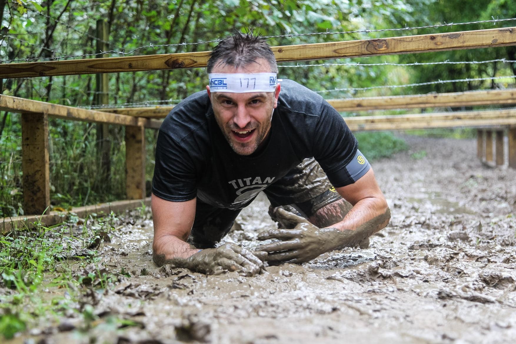 Chris mid-race crawling through mud (and manure!) under barbed-wire netting