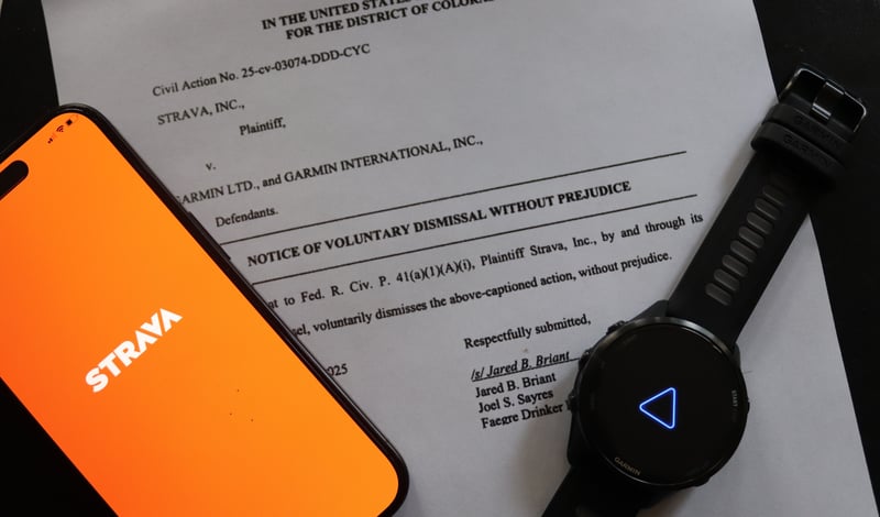 Strava app on a smartphone beside a Garmin Forerunner watch, both resting on a legal document