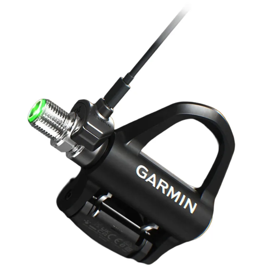 Garmin Rally power meter pedal connecting to magnetic USB-C charging adapter with green LED indicator.
