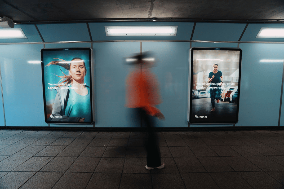 Commuter passing Runna marathon training app billboard ads on the London Underground, Strava-owned coaching platform