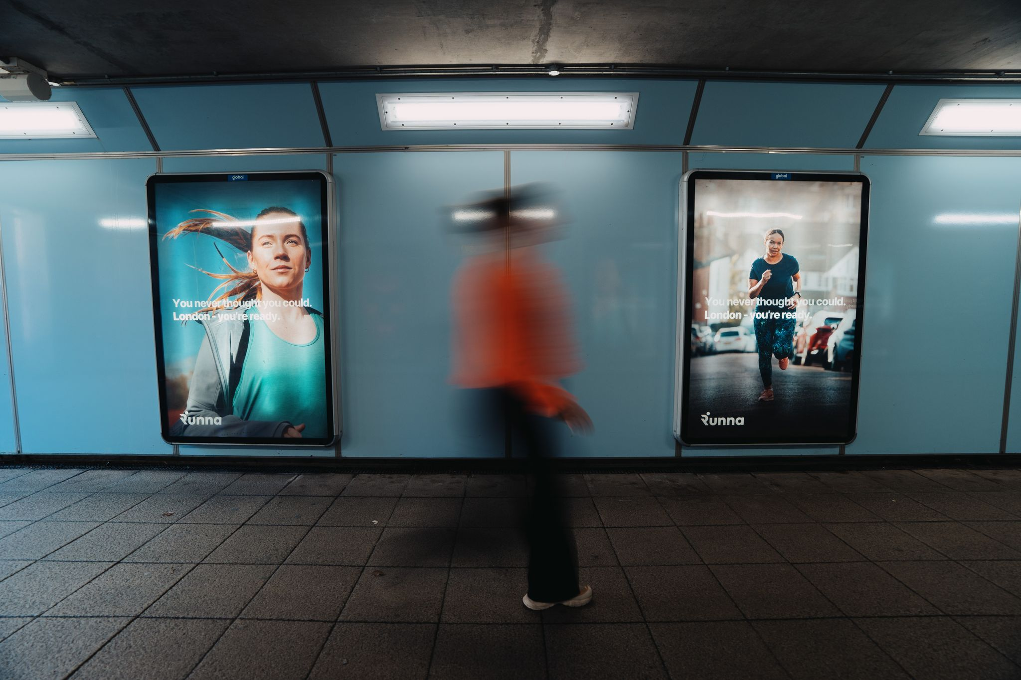 Commuter walking past two Runna training app billboards in a London Underground passageway