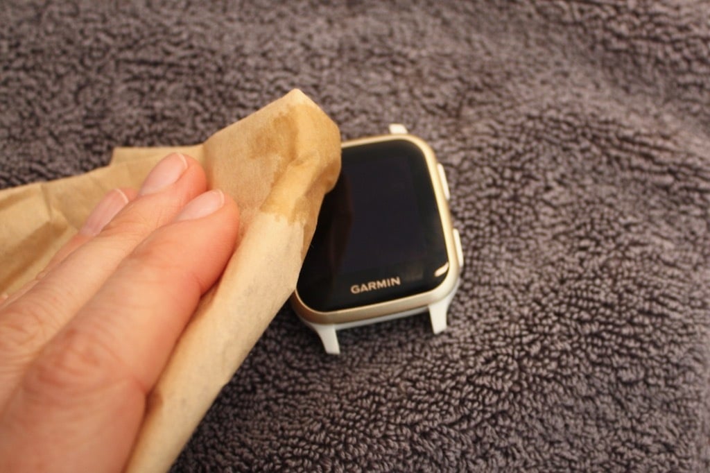 Cleaning a Garmin smartwatch lens with a microfiber cloth before assessing scratch damage