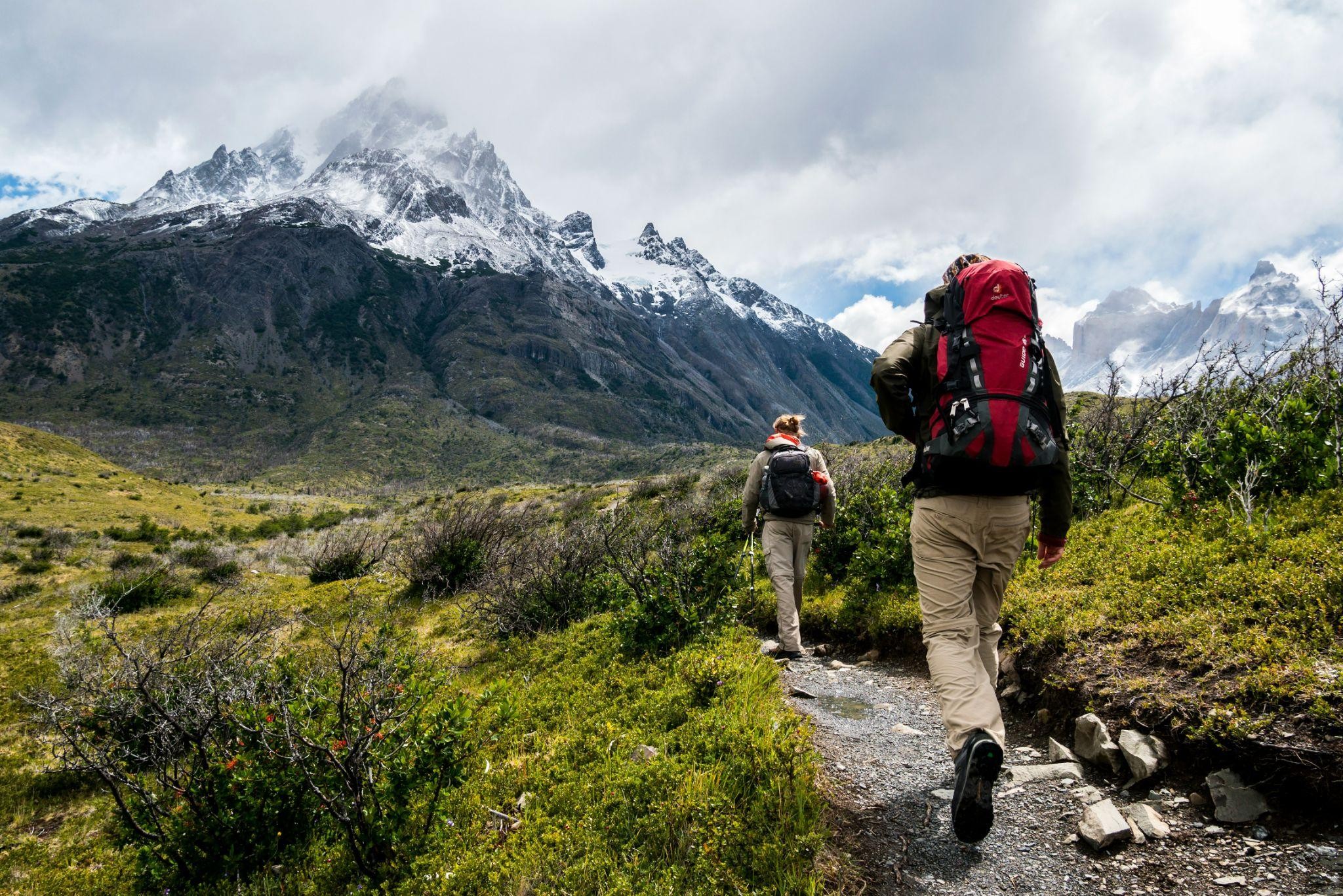 male and female hiker walking up mountain trail with rucksack toward snow covered peak