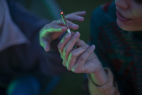 A close-up shot of a woman giving her girlfriend a joint of marijuana