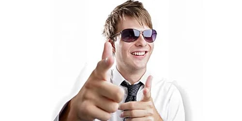 A young white man in a dress shirt and tie displaying finger guns while wearing sunglasses - meant to represent a silly business man. 
