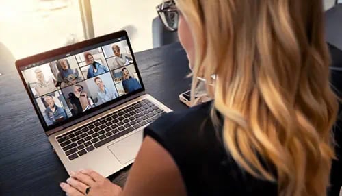 A blond business lady on her laptop, taking a video call with multiple people.