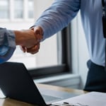 Handdruk boven een bureau met laptop en contract, symbool voor de inhuur van personeel