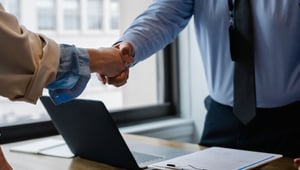 Handdruk boven een bureau met laptop en contract, symbool voor de inhuur van personeel