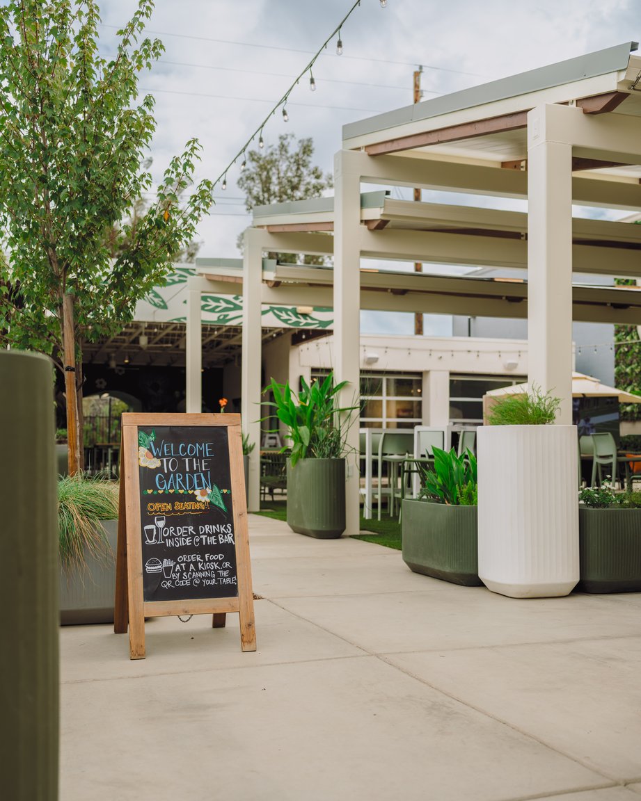 The entrance walkway at The Garden in East Sacramento, with planters, a chalkboard sign and the covered pergola