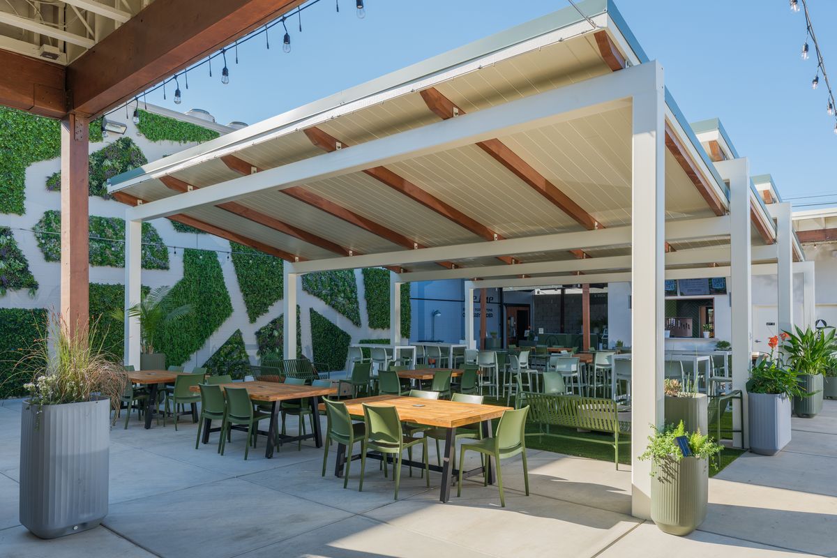 The covered pergola at The Garden in East Sacramento, with wood tables, green chairs and string lights