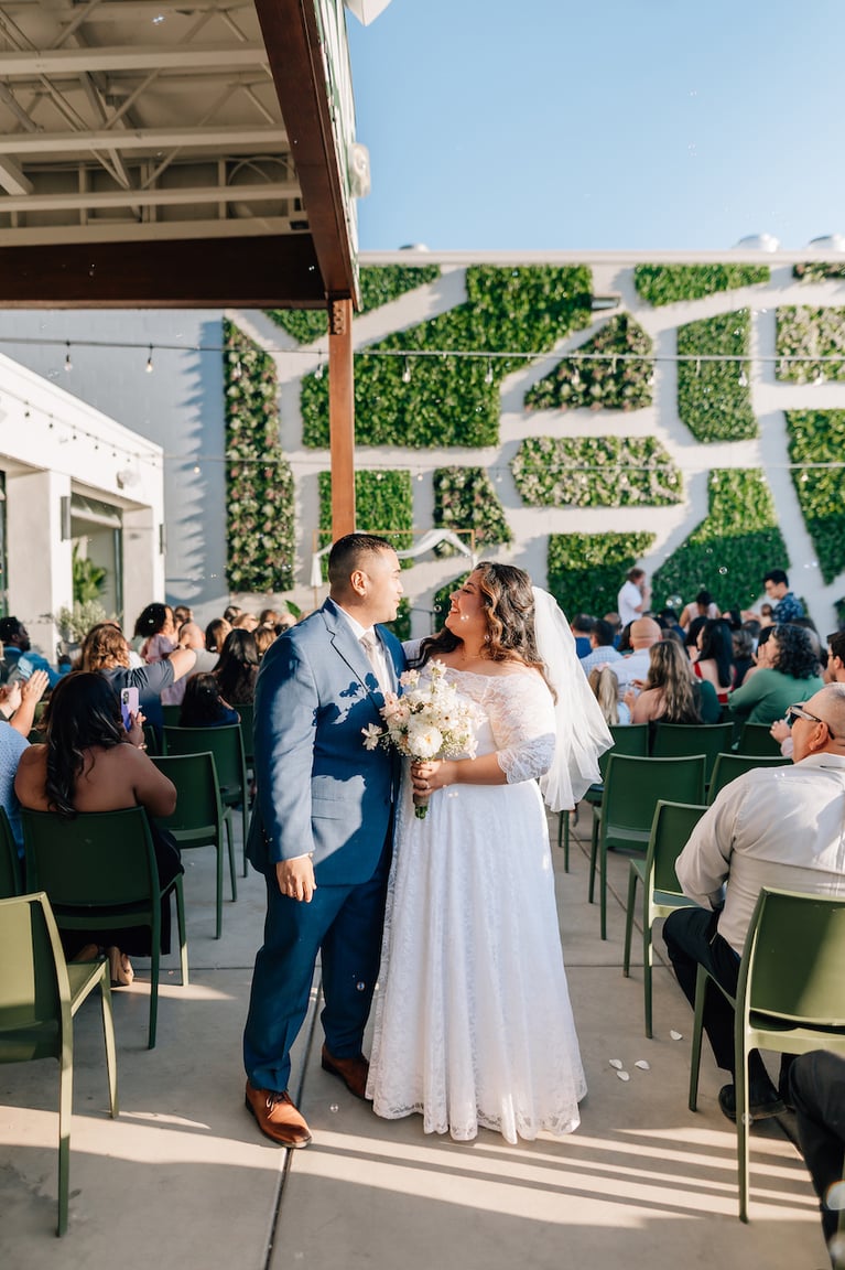 A couple walking down the aisle past their seated guests at a wedding at The Garden