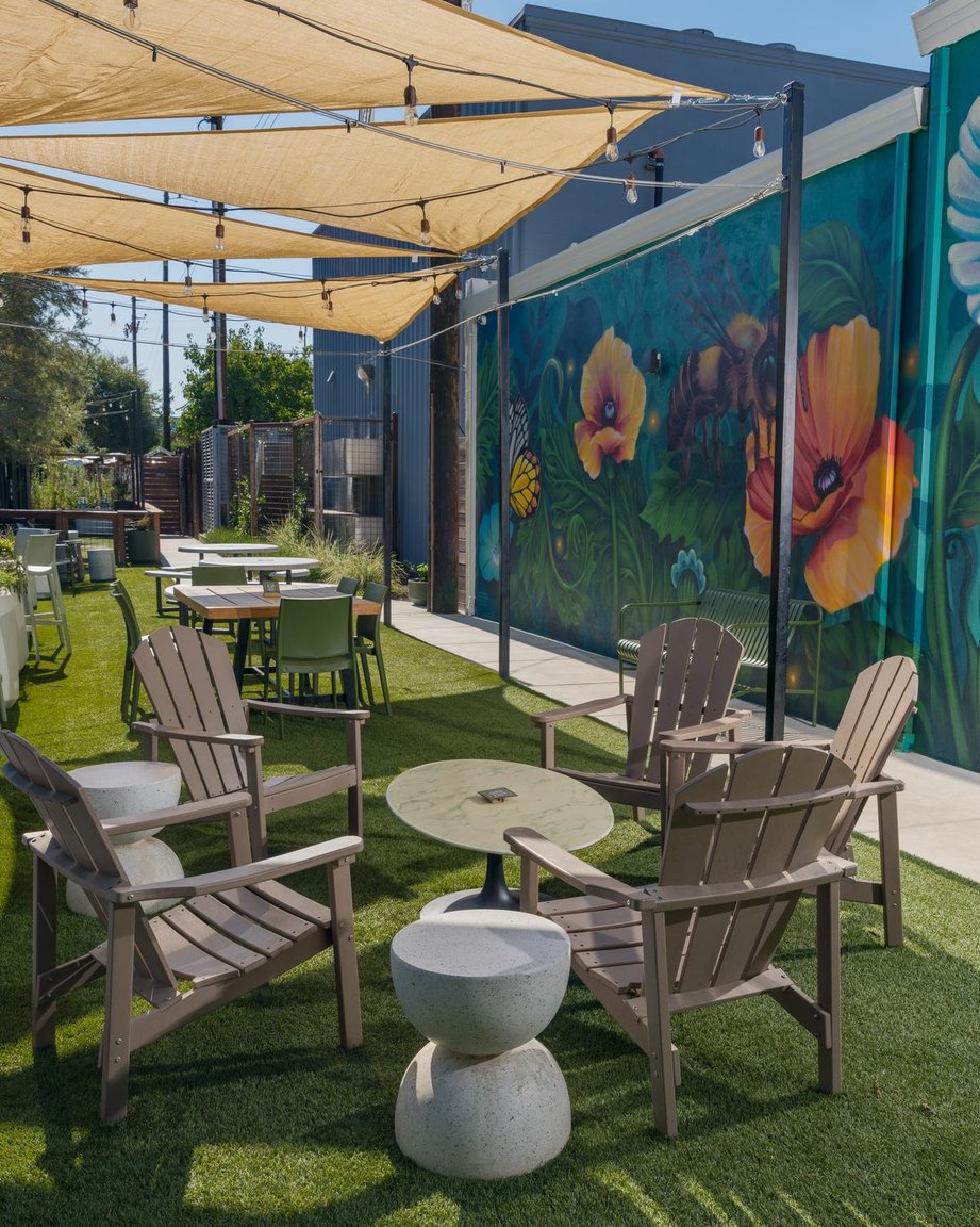 Adirondack chairs under shade sails beside a painted poppy mural in the Back Garden