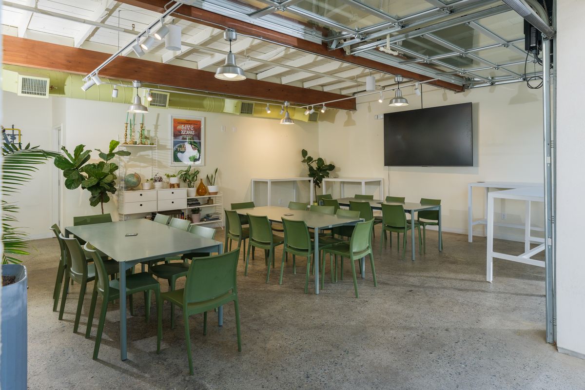 The Garden Room with green tables, a large wall TV and its glass garage door rolled open