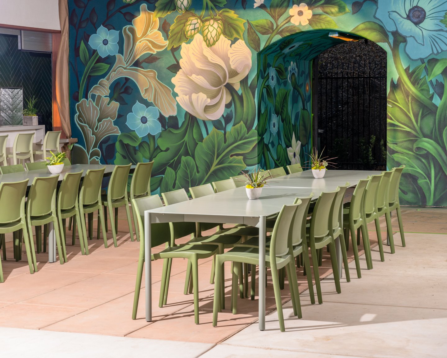 A long table on the covered patio at The Garden in front of a large painted flower mural