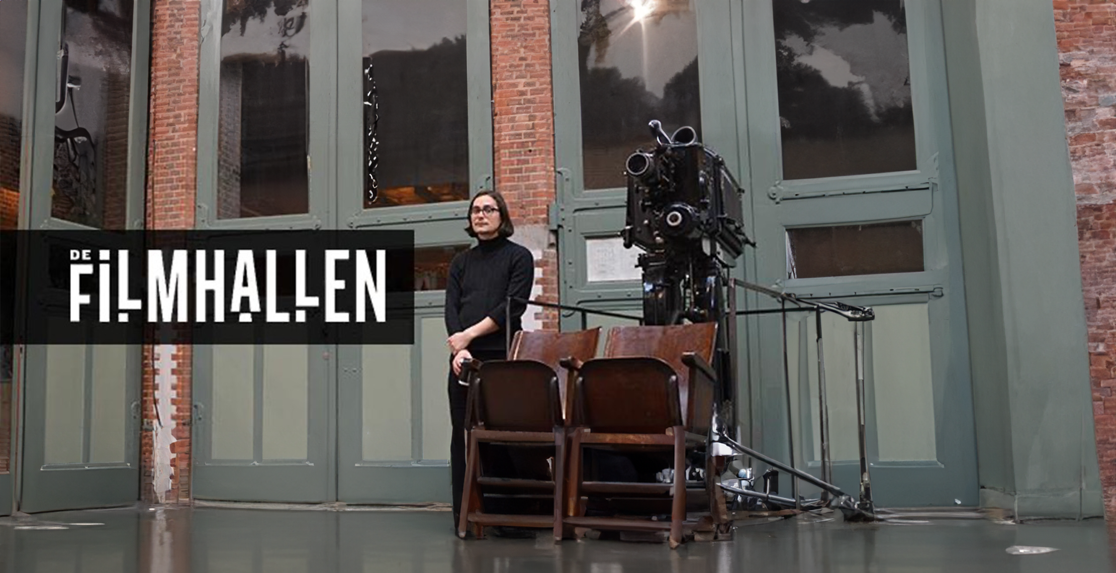 filmhallen logo zichtbaar met foto van person die naast een oude filmprojector en houten filmstoeltjes staat.
