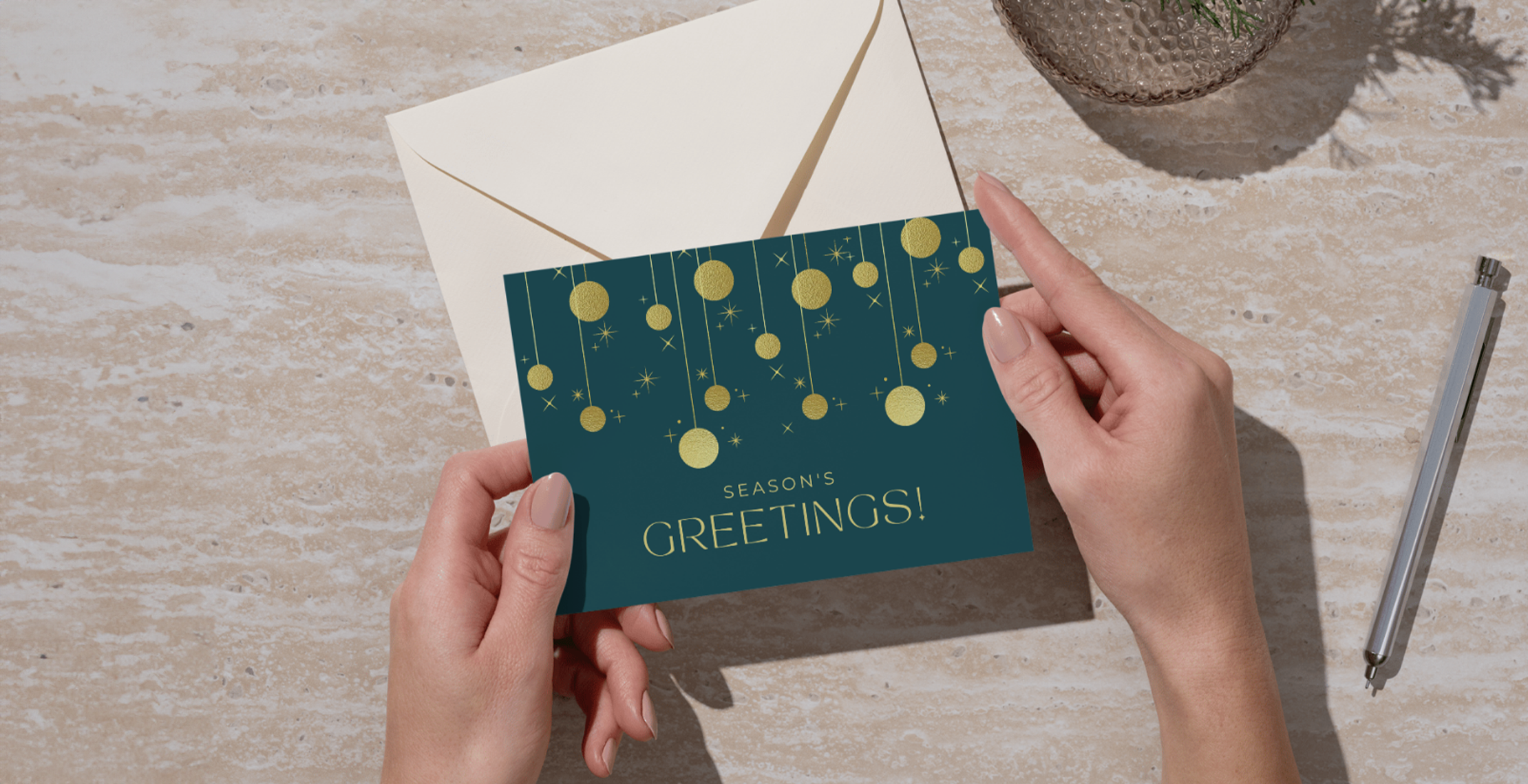 zakelijke kerstkaart met goud foliedruk in de handen van iemand met pen op bureau en envelop op achtergrond