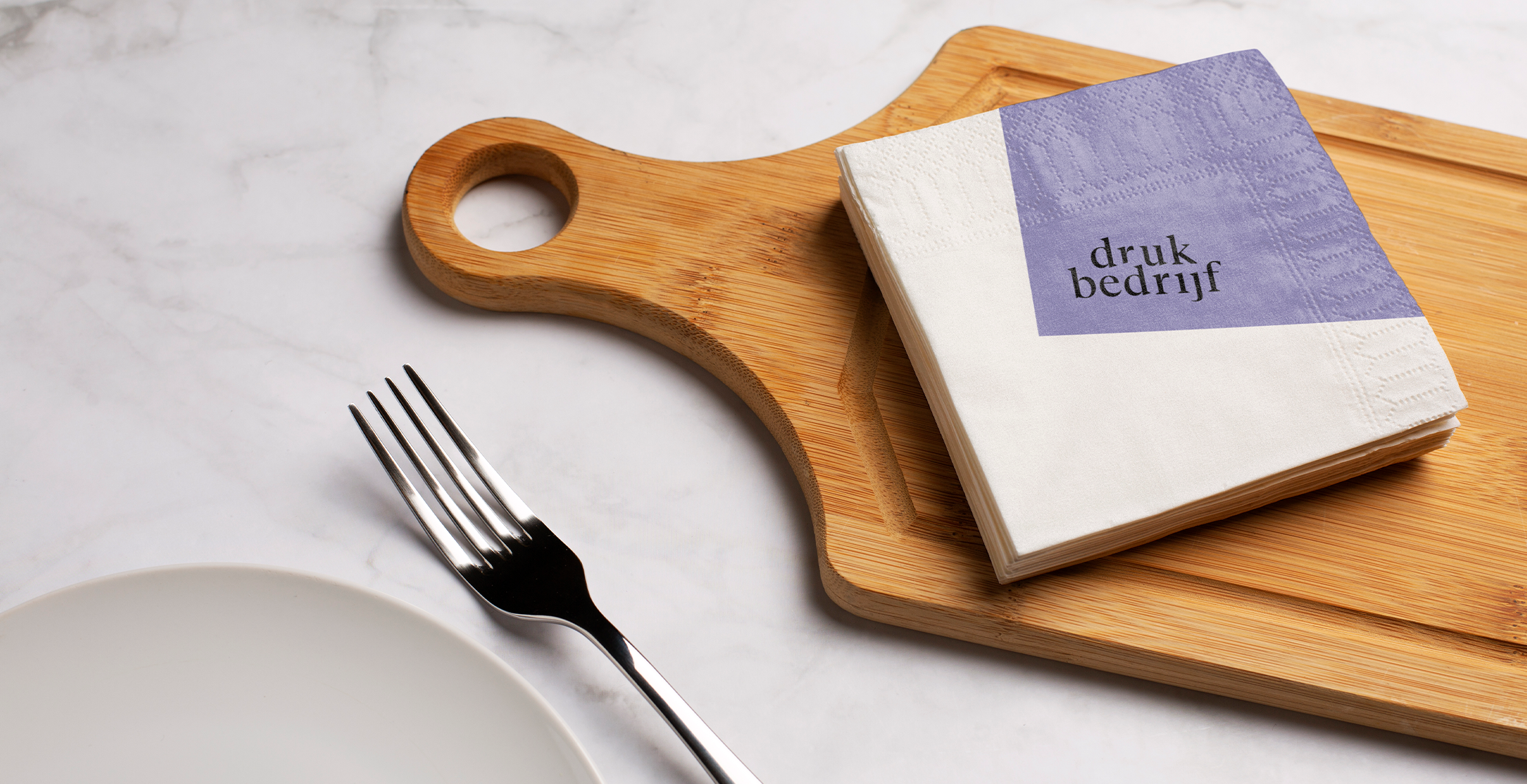 Servet bedrukt met logo op een borrelplank met een vork en bord ernaast. 
