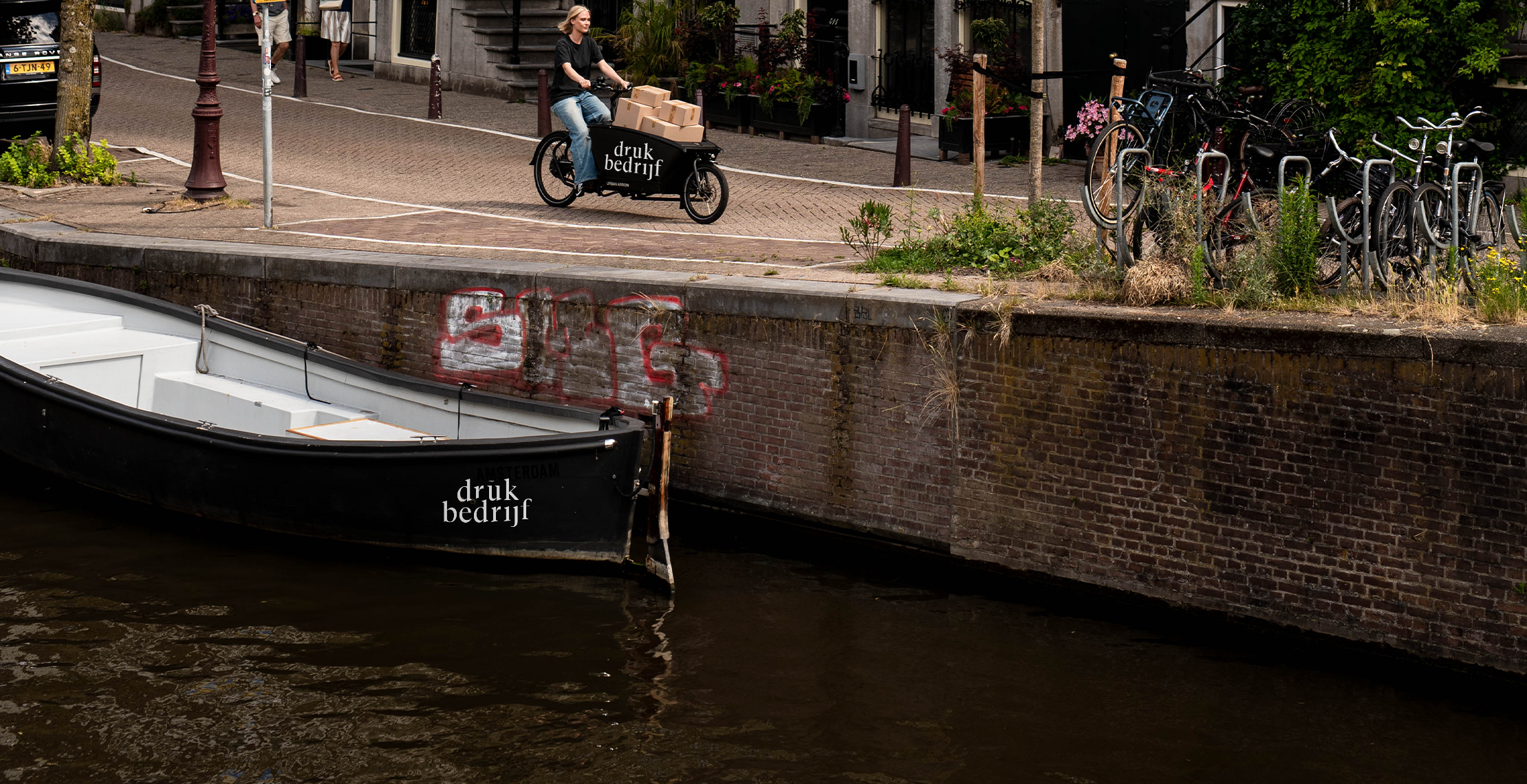 bootbelettering op een sloep in een amsterdamse gracht met daarboven een bedrukte bakfiets
