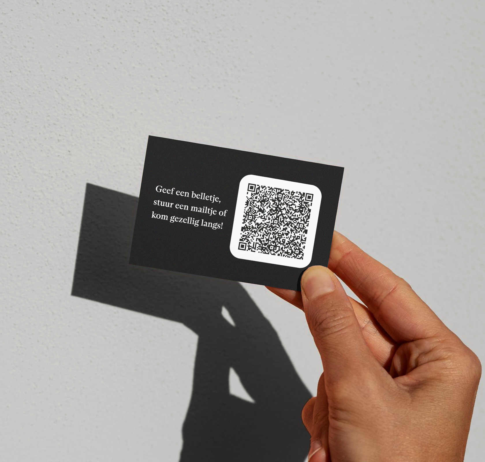 Bedrukt visitekaartje met qr code er op in de hand voor grijze muur.
