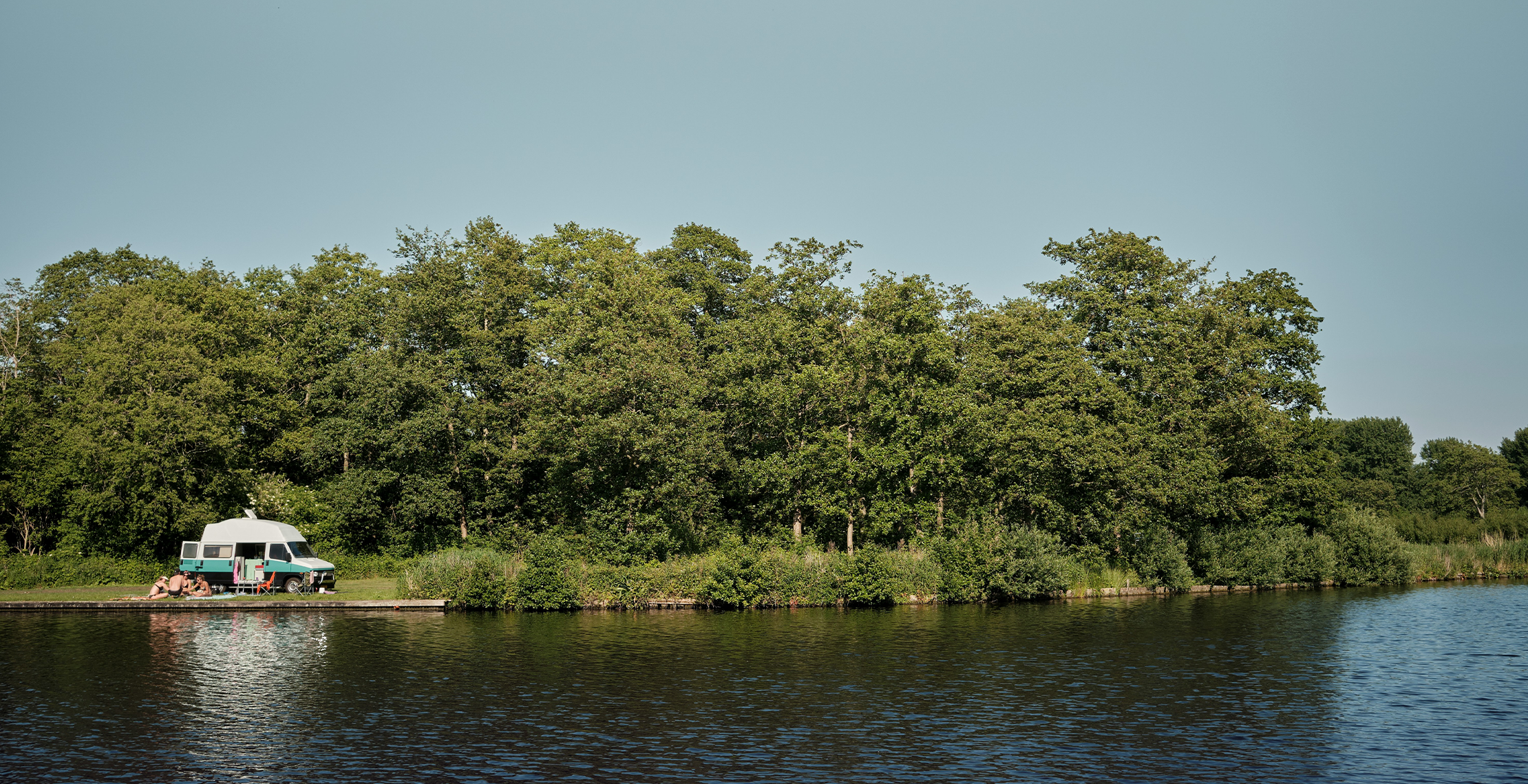 blauwe camper die idyllisch aan de waterkant van een eilandje waar mensen voor picknicken