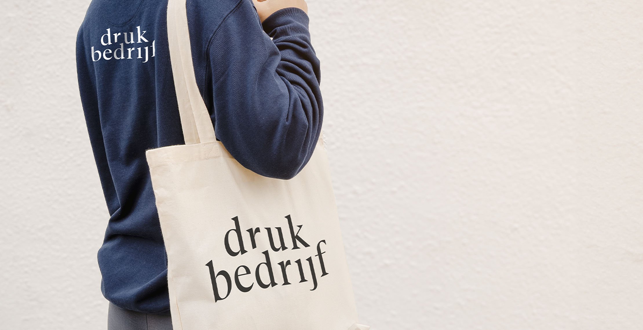 Gepersonaliseerd textiel met je bedrijfslogo van een donkerblauwe bedrukte trui met logo op rug en bedrukte canvas tas met logo