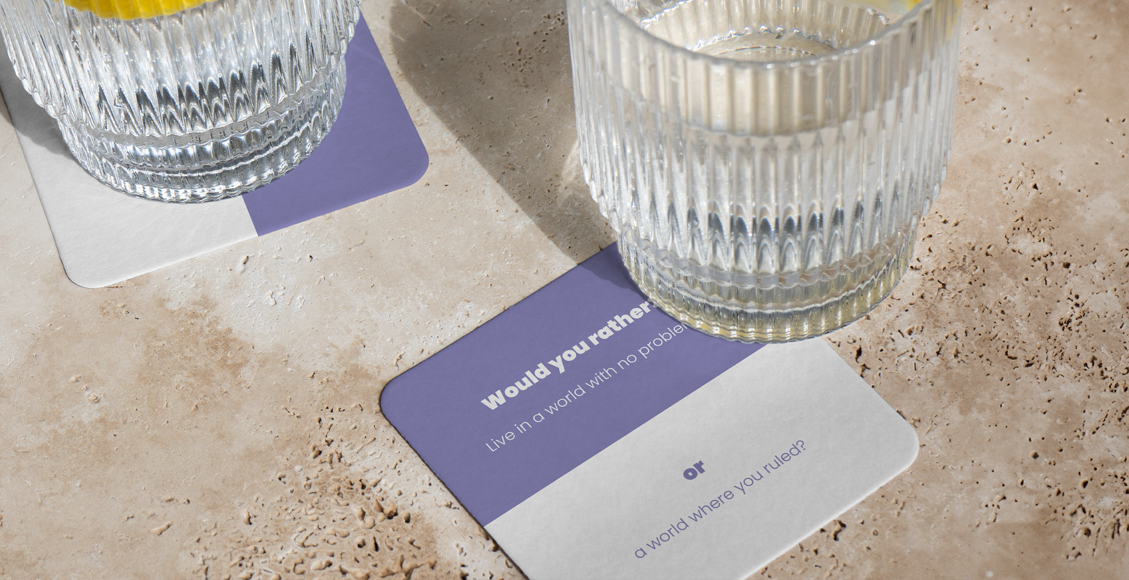 twee bierviltjes bedrukt met interactieve vragen would you rather met daarop glas op een stenen tafel