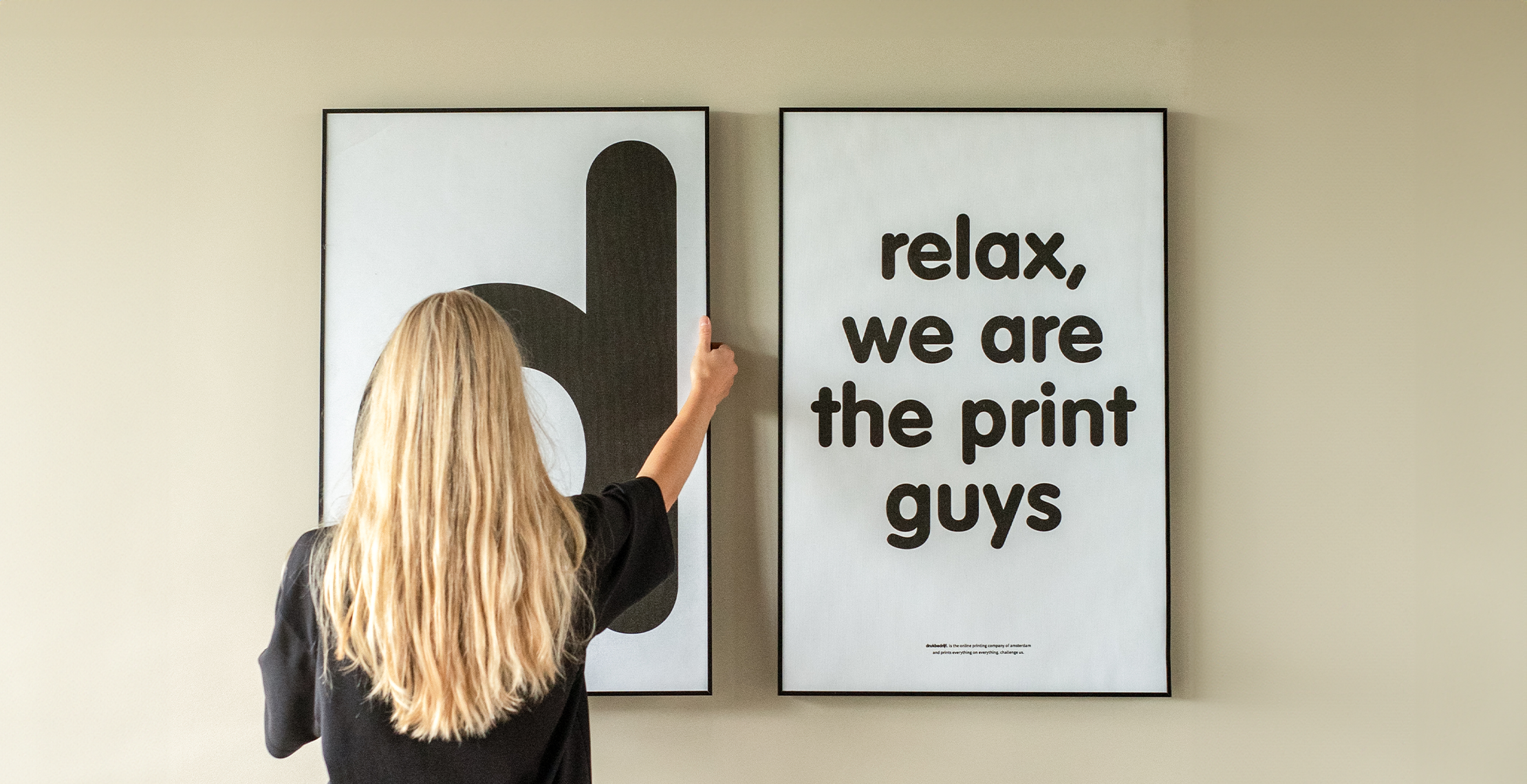 Textielframe aan de muur gehangen met relax we are the print guys op beige muur door blonde vrouw