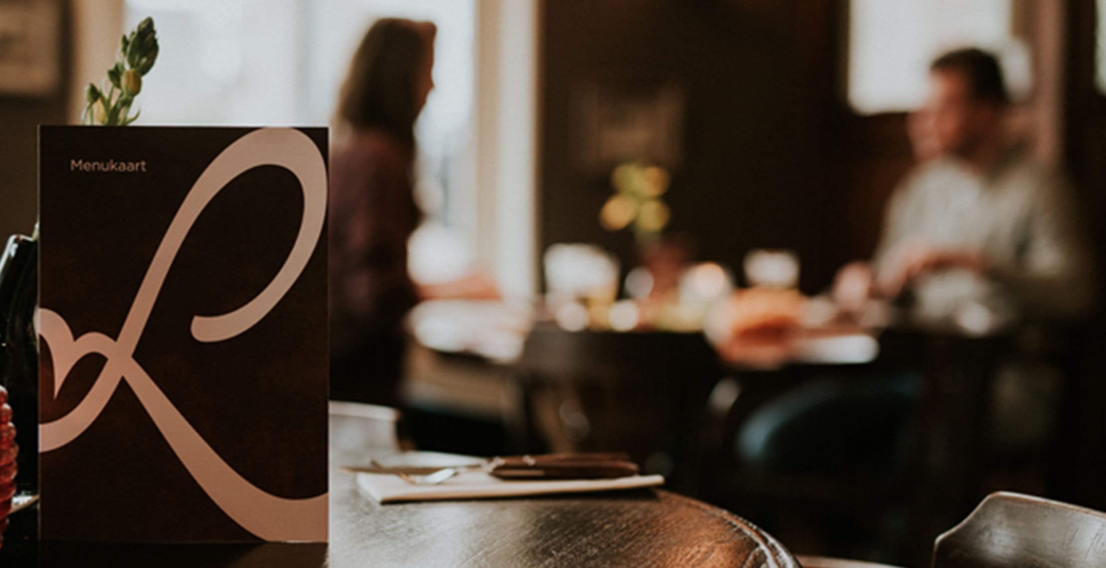 Menukaart van Loetje op tafel met op de achtergrond iemand die aan het eten is. 