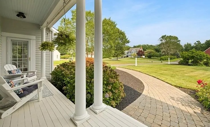Rear porch with white columns and Adirondack chair overlooking a manicured lawn and driveway at a residential home in Lakeville.