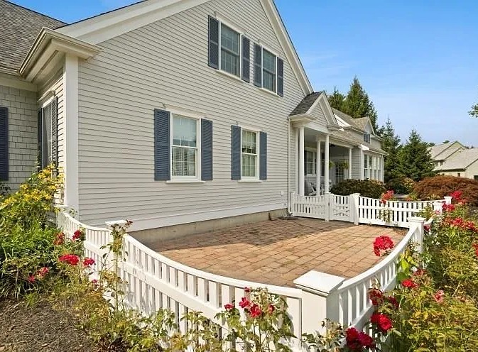 Completed home remodel in Lakeville featuring a two-story house with new light gray vinyl siding, white trim, front porch with columns, and brick paver patio surrounded by white railings and landscaping.
