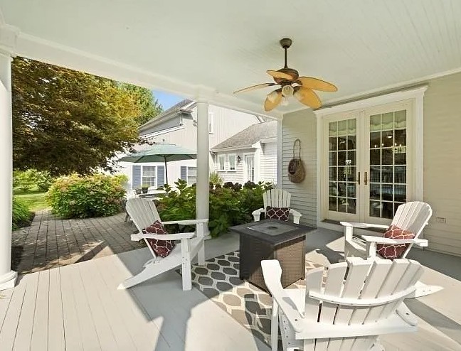 Covered porch with white Adirondack chairs, a fire pit table, ceiling fan, and glass doors opening to a residential backyard in Lakeville.