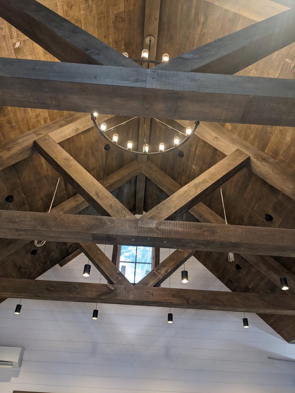 Interior ceiling of a pool house in Lakeville showing exposed wood beams with a chandelier and recessed lighting.