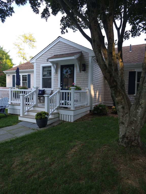 A new mudroom addition with white railings and covered entry extends from the side of a gray shingled house in Marion.