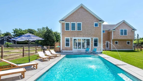 Back view of a residential home with pool and patio area featuring lounge chairs and an umbrella.