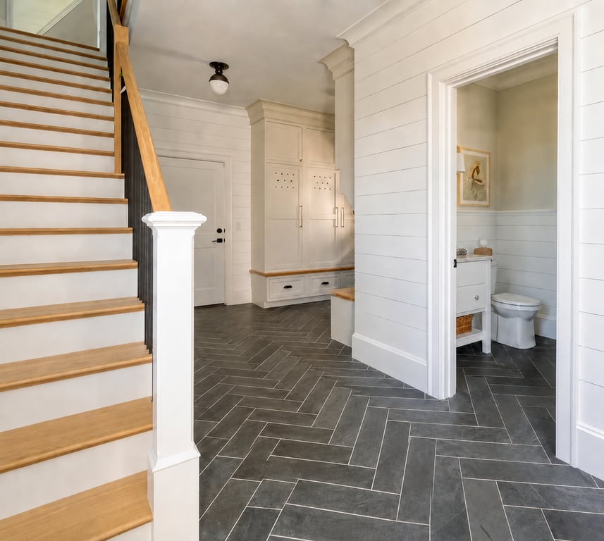 Finished mudroom with herringbone tile flooring, built-in cabinetry with open shelving, white shiplap walls, wooden stair railing, and an adjacent half bath.