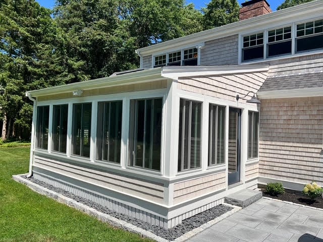 A white-framed sun porch addition with multiple large windows and glass doors attached to a shingled house in Marion.