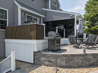 Finished backyard deck and patio area with outdoor kitchen, grill, pergola, and seating area attached to a residential home.