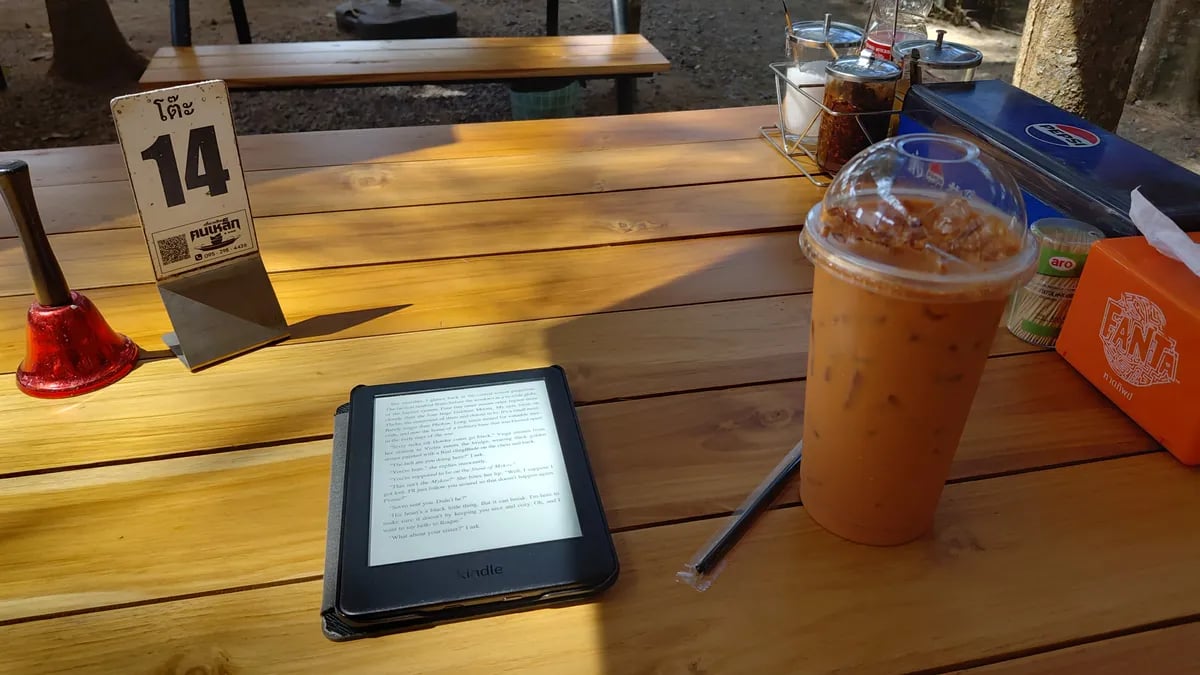 A cafe table in the sun with an e-reader and Thai iced tea