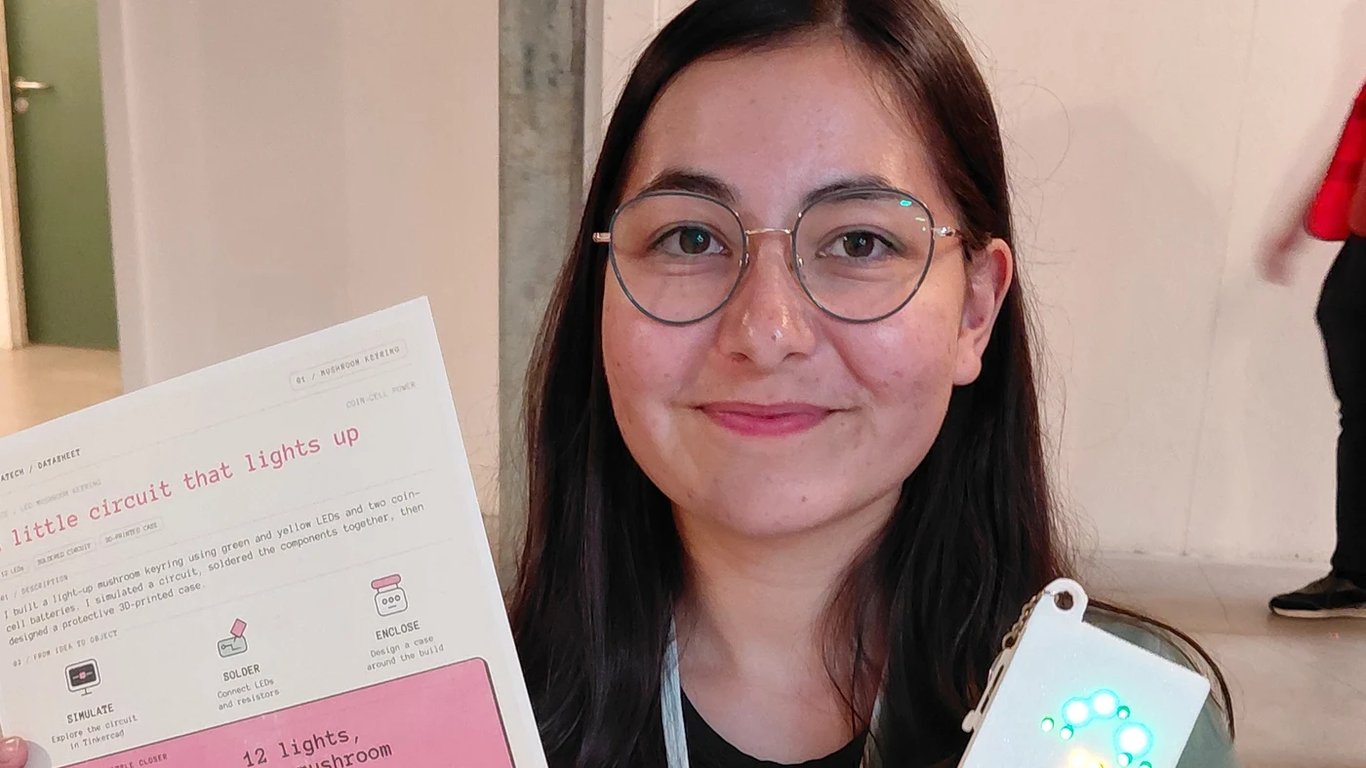 Tikita holding the illuminated mushroom LED keyring beside its project datasheet