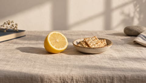 A halved lemon and a small dish of plain crackers, on cream linen in soft window light
