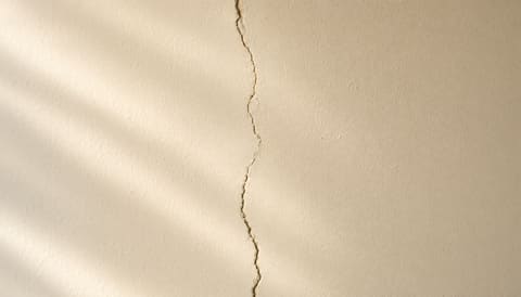 A vertical structural crack running top to bottom of a cream wall surface
