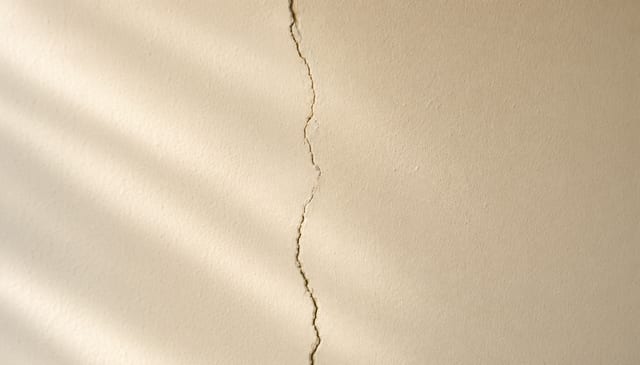 A vertical structural crack running top to bottom of a cream wall surface