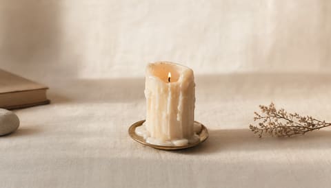 A single candle nearly extinguished, with melted wax pooled at its base, on cream linen