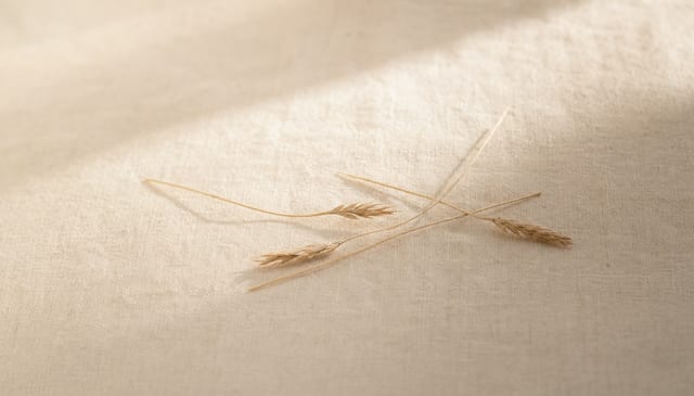 A few loose, dry-grass strands resting on cream linen