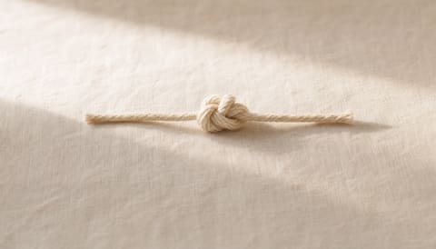 A tightly tied knot in cream string resting on cream linen — visual metaphor for head pressure