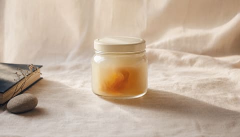 A sealed cream-glass jar with subtly visible amber interior on cream linen — internal-vs-external metaphor