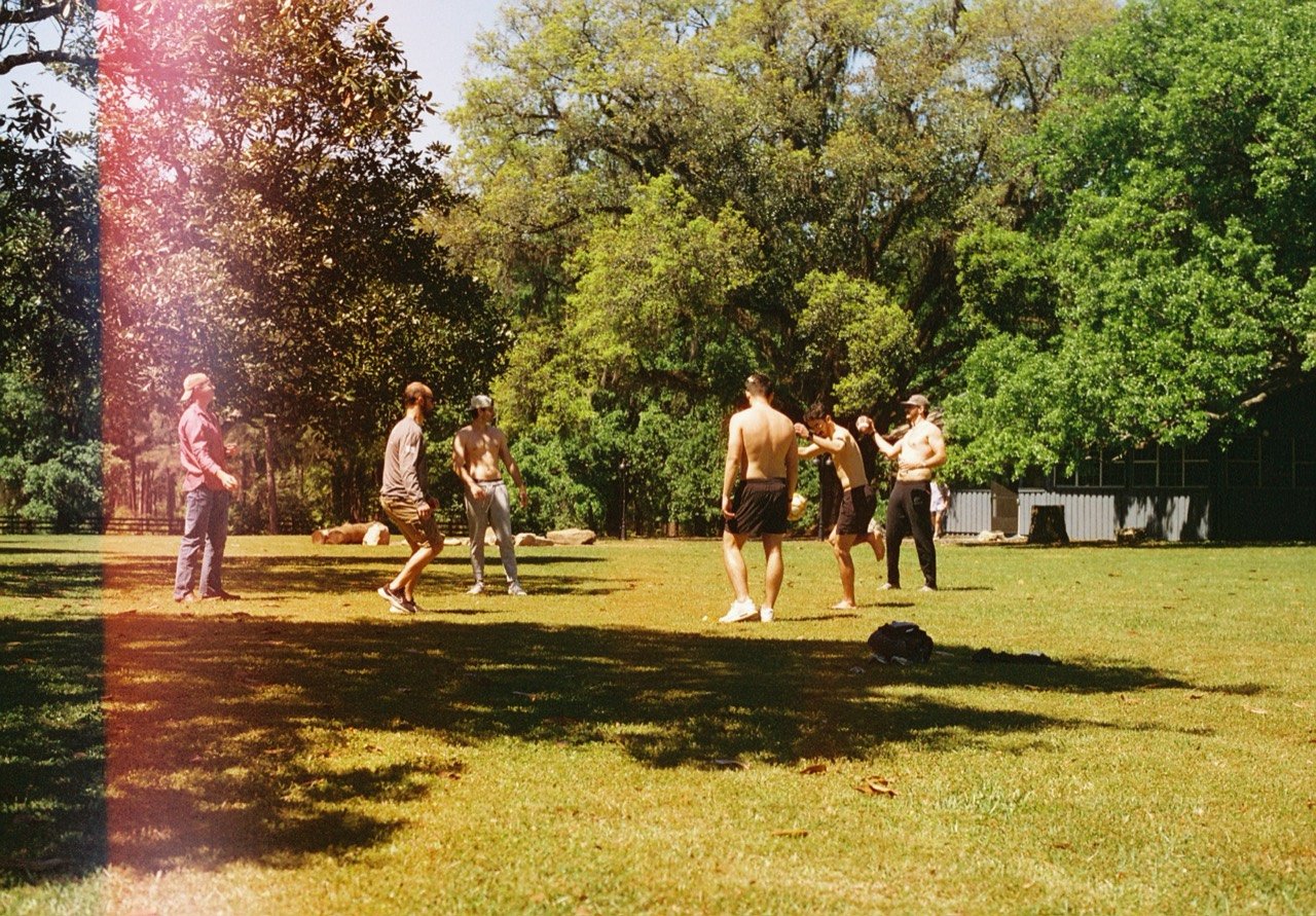 Groomsmen playing soccer on the lawn with a pink light leak along the edge of the film photograph.